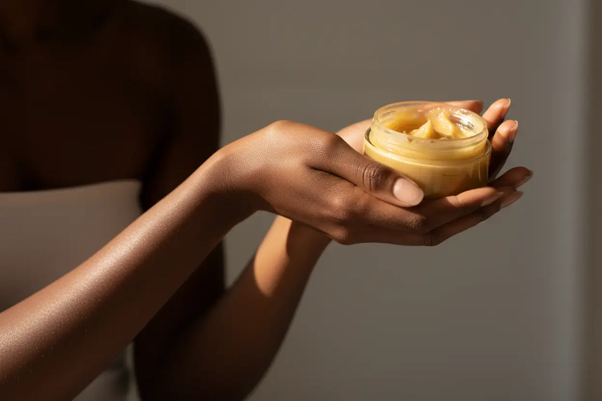 A woman with naturally glowing, radiant skin, holding a jar of unrefined shea butter as her secret for a natural body glow.